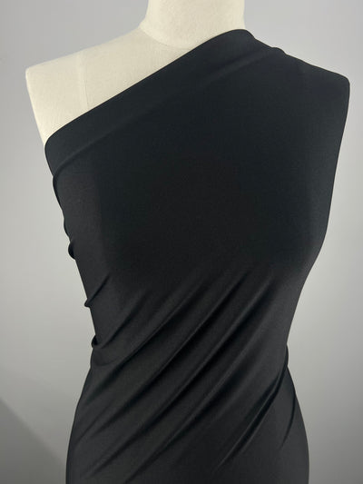 On display is an elegant off-the-shoulder dress crafted from the Plain Lycra – Black by Super Cheap Fabrics. This form-fitting garment features a one-sleeve design, gracefully draping down the body to highlight simple and sophisticated lines, making it an ideal choice for a comfortable yet stylish wardrobe.