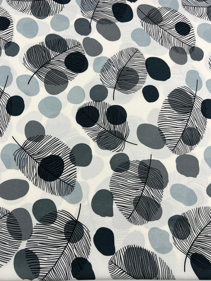 Introducing Super Cheap Fabrics' Printed Crepe - Black Dotty Leafs - 150cm: A lightweight, high-fashion fabric adorned with intricate black and grey leaves interspersed with circles of various sizes in shades of blue, grey, and black on a white background. The design features fine lines that create a delicate, nature-inspired aesthetic.