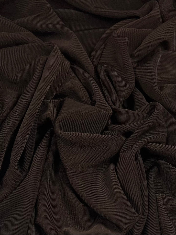 A close-up of Slinky Knit - Chocolate - 135cm by Super Cheap Fabrics with visible ribbed texture, gathered and draped in soft folds and wrinkles. The medium-weight material appears soft and plush, displaying its characteristic horizontal lines and creating a sense of depth and richness.