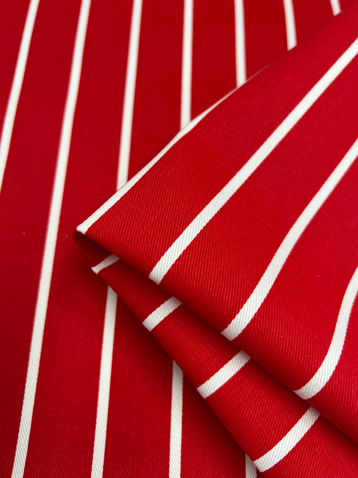 A close-up image of Super Cheap Fabrics' Denim - Bold Red - 155cm with white vertical stripes. The medium weight fabric is neatly folded, showcasing its smooth texture and vibrant colors.