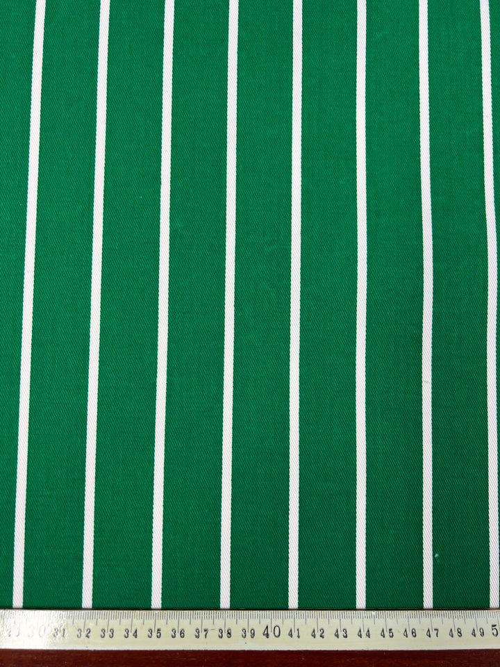 Green and white fabric with evenly spaced vertical stripes. A measuring tape at the bottom shows a width of approximately 45 centimeters. This 100% cotton, medium weight fabric maintains a consistent pattern throughout. Introducing: **Denim - Bold Green - 155cm** by **Super Cheap Fabrics**.