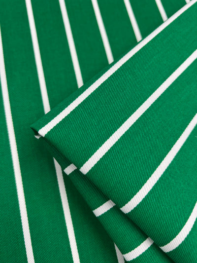 Close-up of Super Cheap Fabrics' Denim - Bold Green - 155cm with white diagonal stripes. The medium weight fabric is folded, showing the pattern clearly on both layers with crisp, parallel lines. The texture of the fabric is visible, indicating a sturdy and durable material ideal for children's clothing.