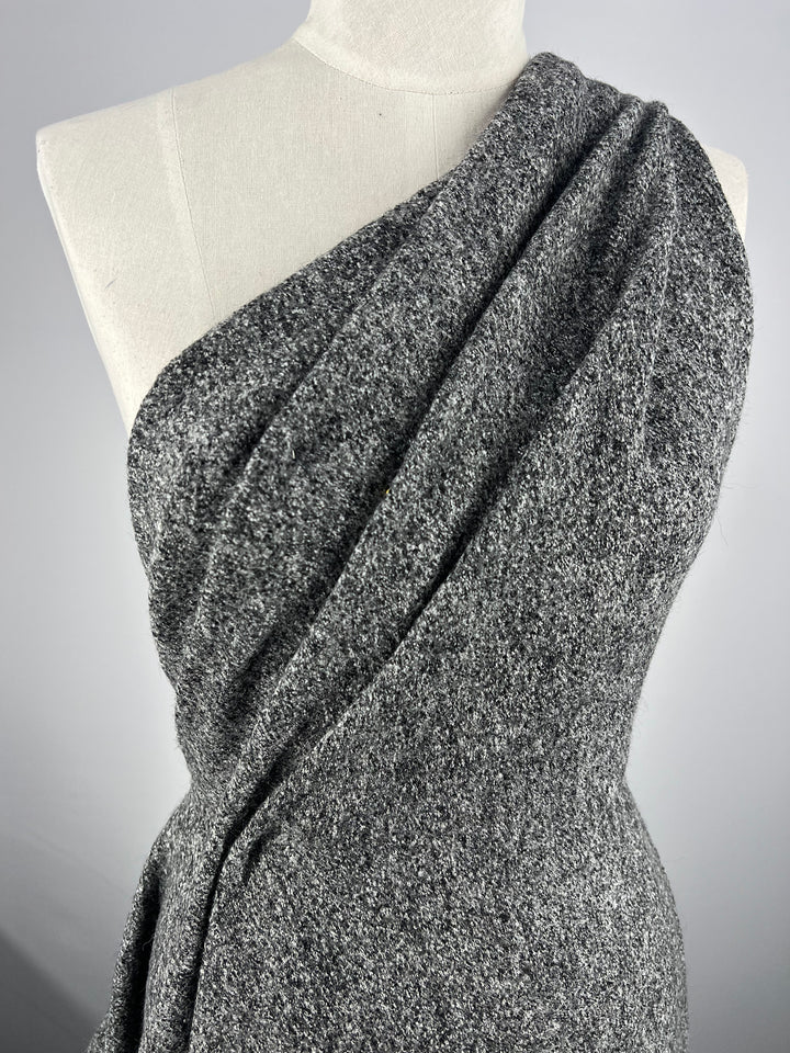 A close-up of a mannequin wearing a textured grey off-shoulder top made from Super Cheap Fabrics' Boiled Wool - Grey Marle - 140cm. The fabric drapes diagonally across the front, creating a stylish and elegant look perfect for Autumn/Winter clothing. The background is plain and grey, highlighting the garment.