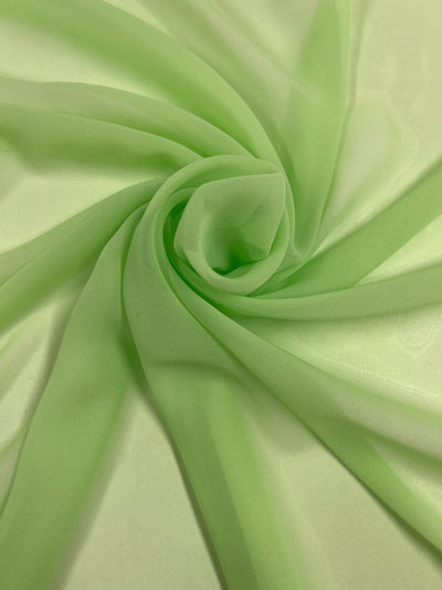 A delicate piece of light green Hi-Multi Chiffon - Butterfly - 150cm fabric from Super Cheap Fabrics is artfully draped and gathered in a swirling pattern. The material is translucent and smooth, with gentle folds radiating from the center, creating a soft, elegant look reminiscent of Sugar Coral.