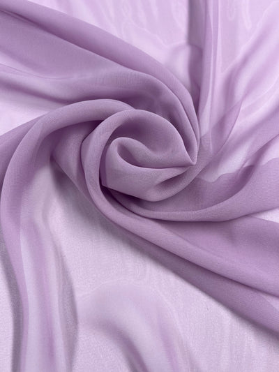 A close-up image of light purple, lightweight Hi-Multi Chiffon - Bleached Mauve - 150cm fabric by Super Cheap Fabrics arranged in soft folds, creating a swirling pattern. The texture appears smooth and silky, reflecting light subtly to showcase its delicate appearance—perfect for floaty tops.