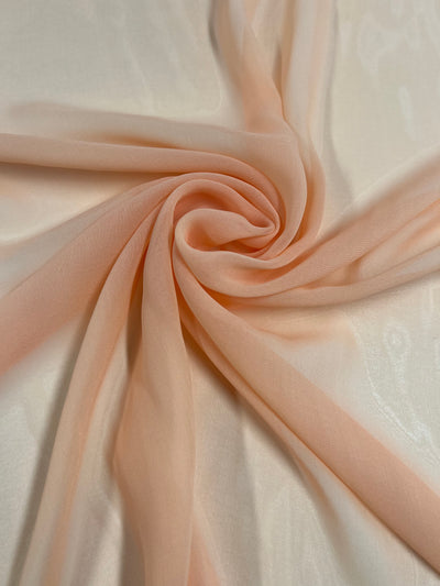A close-up photograph of Hi-Multi Chiffon - Cream Tan - 150cm by Super Cheap Fabrics, swirled in a circular pattern. The material appears translucent and has a delicate texture, with light reflections adding a subtle sheen to the sheer fabric.