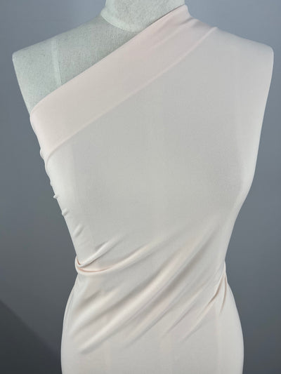 Close-up of a mannequin dressed in an asymmetrical, medium weight, one-shoulder dress. The Super Cheap Fabrics ITY Knit - Baby Pink - 150cm fabric is smooth and drapes elegantly with subtle ruching on the side, creating a sleek and refined look. The background is plain and gray, keeping the focus on the dress.