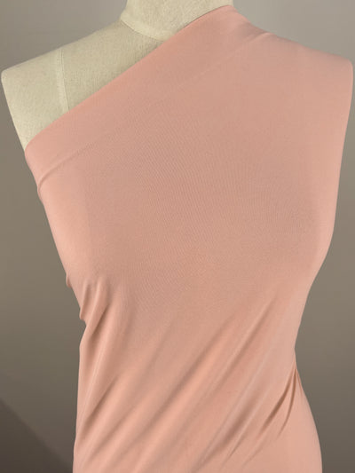A close-up image of a peachskin-colored, one-shoulder dress on a mannequin. The medium-weight fabric, Super Cheap Fabrics' ITY Knit - Peachskin - 150cm, has a smooth texture and drapes elegantly, with the shoulder detail visible. The background is plain and neutral, highlighting the garment beautifully.