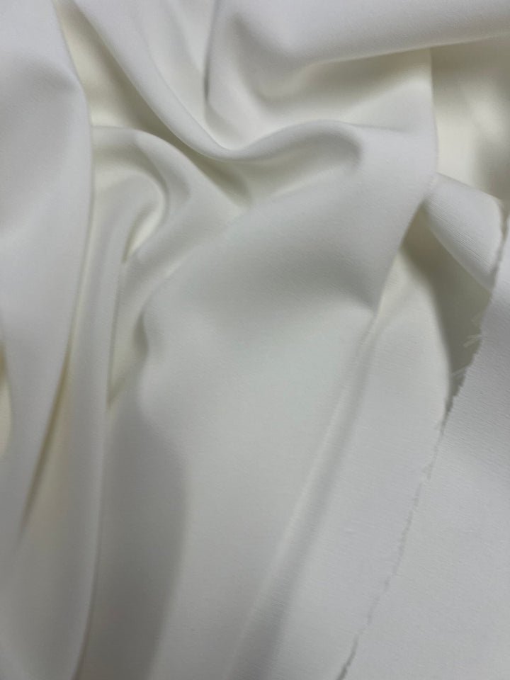A close-up photo of Super Cheap Fabrics' Stretch Suiting - Ivory - 150cm with soft folds and gentle light reflections. The fabric appears silky and has a slight sheen, showcasing its delicate texture and drape, perfect for sophisticated evening wear.