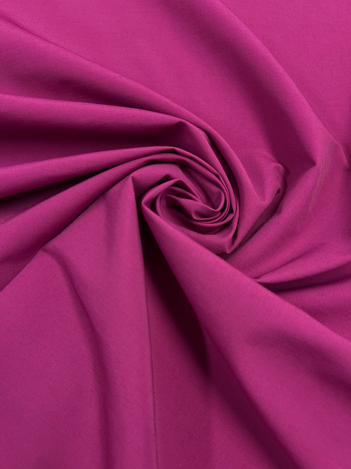 A close-up of a wrinkled polyester cotton blend fabric in a rich, magenta color. The lightweight fabric is swirled in the center, creating a visually appealing texture and pattern reminiscent of Poplin - Cactus Flower - 152cm by Super Cheap Fabrics. The surface appears smooth and soft.