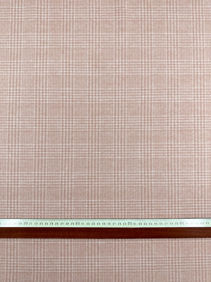 A close-up of a fabric with a pink and white checkered pattern. At the bottom of the image, there is a measuring tape and a straight edge, both extending horizontally across the heavyweight fabric. The measuring tape shows measurements in centimeters. The fabric depicted is Wool Flannel - Coral - 148cm by Super Cheap Fabrics.