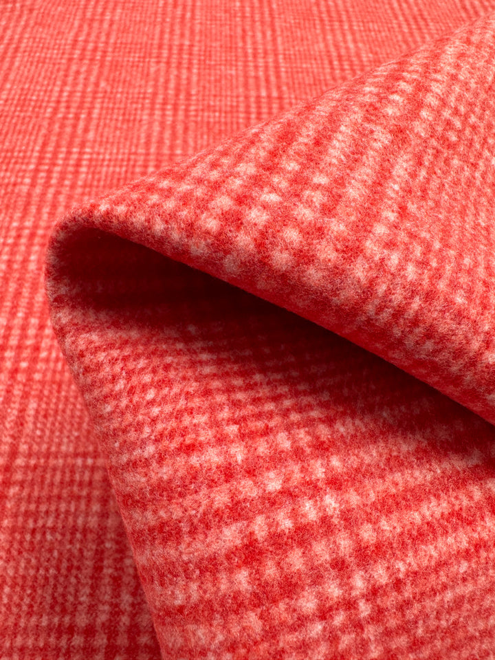 A close-up image of a piece of Super Cheap Fabrics Wool Flannel - Dubarry - 148cm folded slightly over itself. The fabric has a red and white plaid pattern, with a soft, fuzzy texture often found in cozy jackets. The intersecting lines create a checkered grid effect, focusing on the detailed texture and pattern.