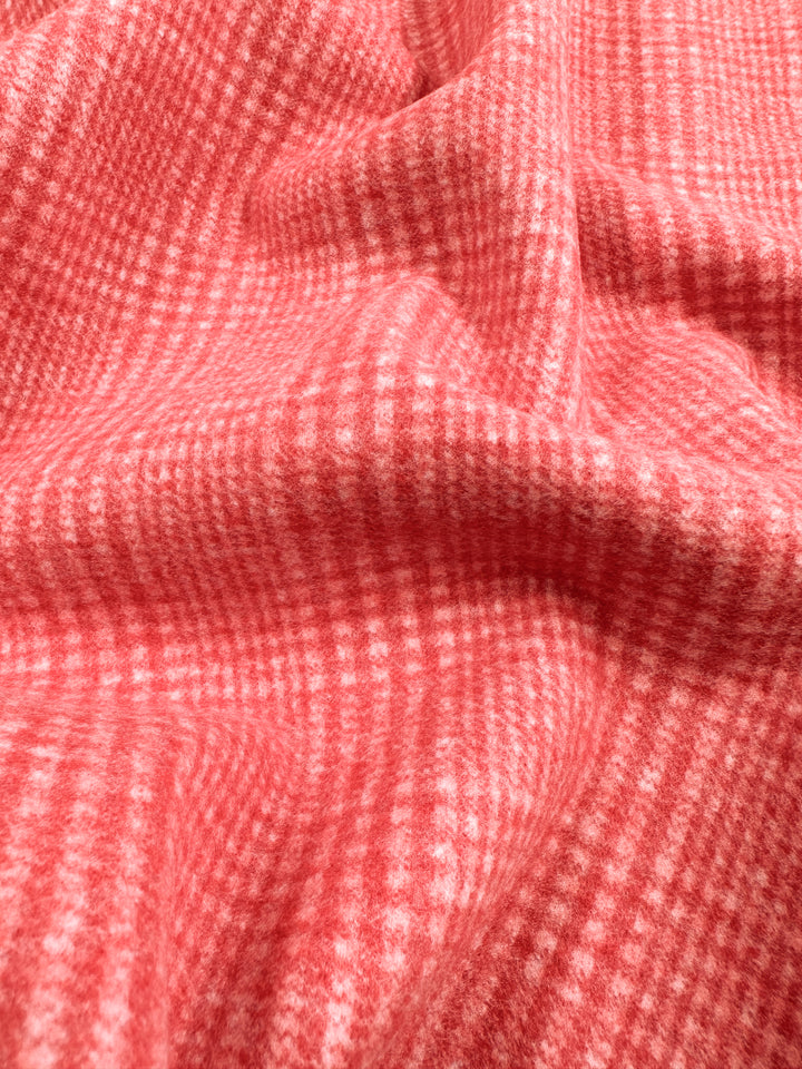 A close-up view of a red and white textured fabric with a gingham checkered pattern. The heavyweight fabric is draped, creating soft folds and shadows, highlighting the alternating squares of color—a perfect choice for stylish jackets and coats. This is the Wool Flannel - Dubarry - 148cm by Super Cheap Fabrics.