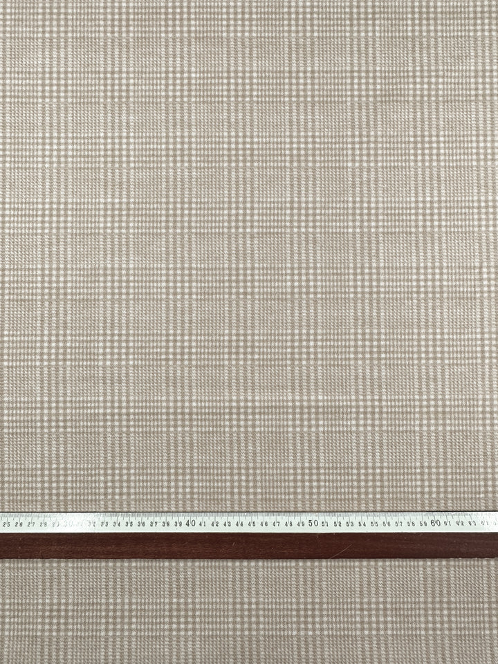 A close-up view of a beige and white plaid wool blend fabric pattern with a ruler at the bottom edge for scale. The numbers on the ruler are legible from 20 to 60, indicating the measurement in centimeters, making it perfect for coats and jackets. This is Wool Flannel - Macchiato - 148cm by Super Cheap Fabrics.