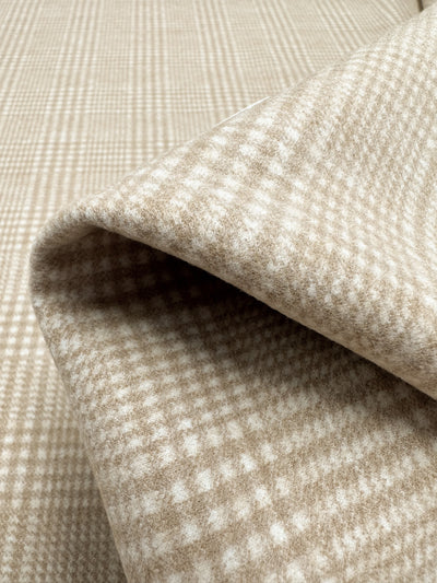 A close-up view of **Wool Flannel - Macchiato - 148cm** by **Super Cheap Fabrics**, showing its texture and pattern. The fabric is partially folded, revealing a soft, woven design with intersecting lines creating a checkered appearance, ideal for cozy coats and jackets.