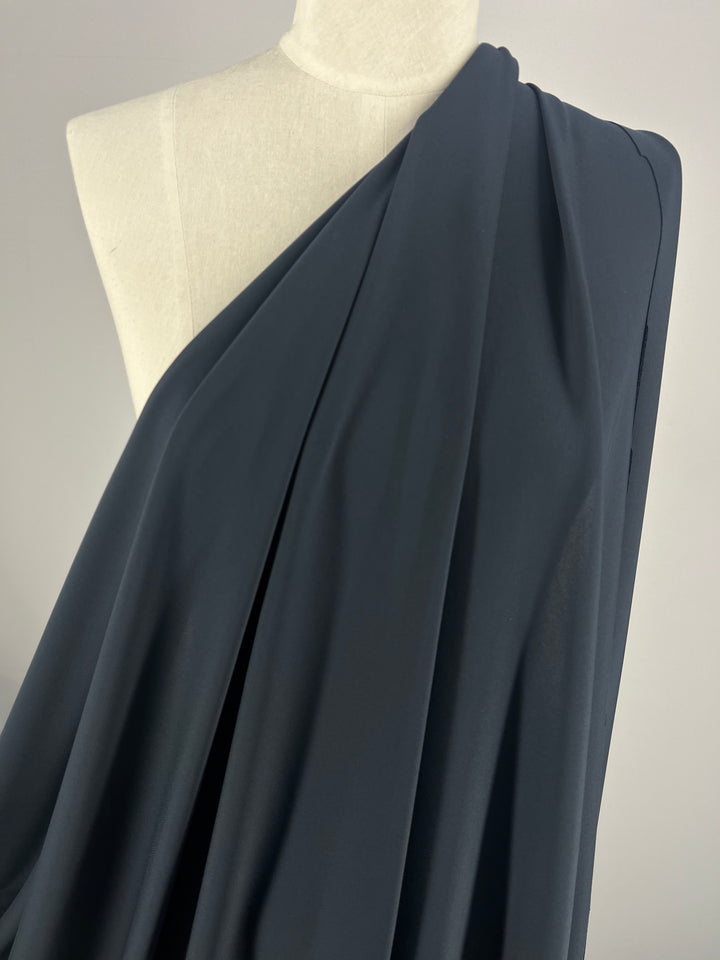 A navy double knit jersey from Super Cheap Fabrics drapes gracefully on the mannequin, creating gentle folds and an elegant look. This medium weight fabric is arranged asymmetrically over the shoulder, enhancing its soft elasticity against a neutral background.