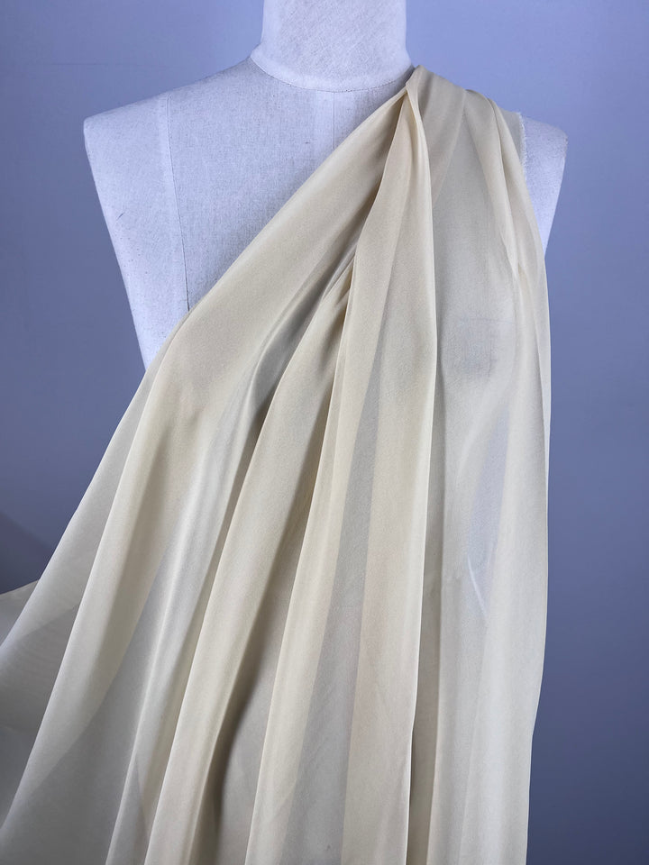 A Super Cheap Fabrics mannequin highlight features Pure Silk Georgette in Gold, gracefully draping over one shoulder, set against a muted gray backdrop.