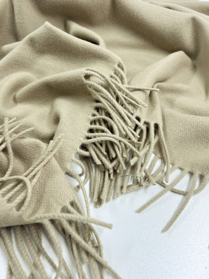 A 140cm panel of pale olive green fabric from Super Cheap Fabrics, crafted in Merino wool, features a soft texture and fringed edges. It appears warm and cozy with a simple yet stylish design, offering excellent moisture-wicking properties.