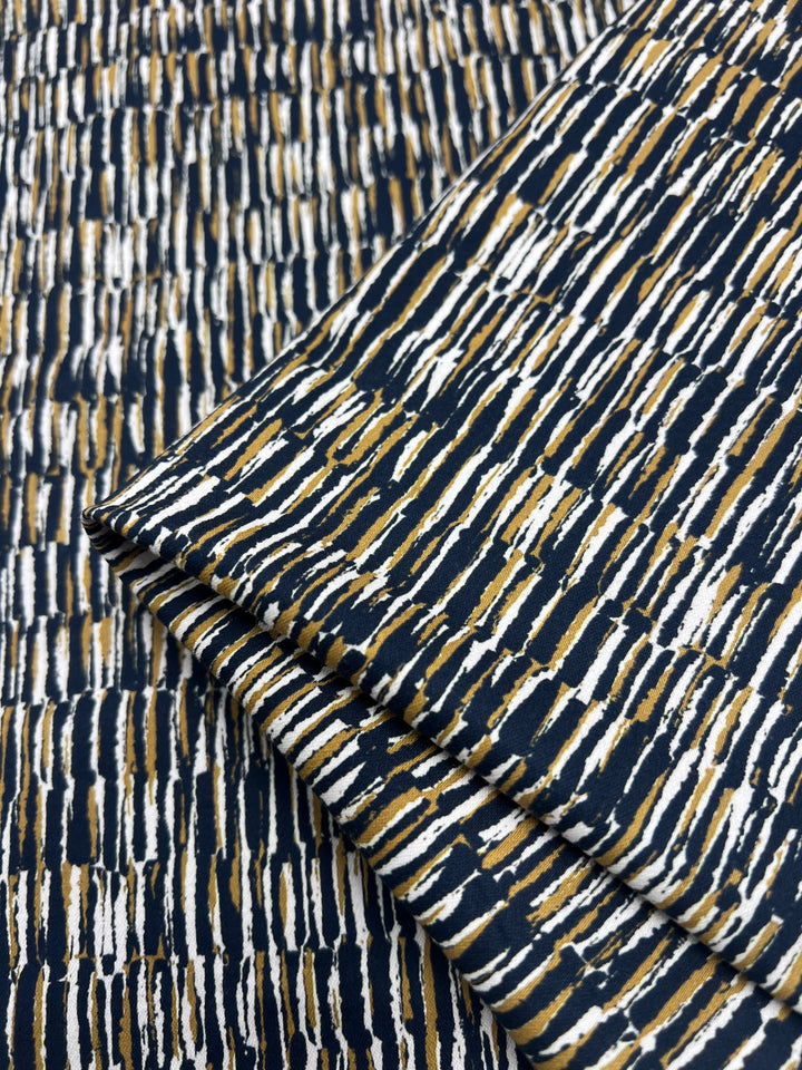 Close-up of folded Cotton Sateen - Eclectic fabric, featuring an abstract pattern with horizontal streaks in white, ochre, and black. This textured design by Super Cheap Fabrics offers comfort and stretch in a 145cm cotton elastane blend.