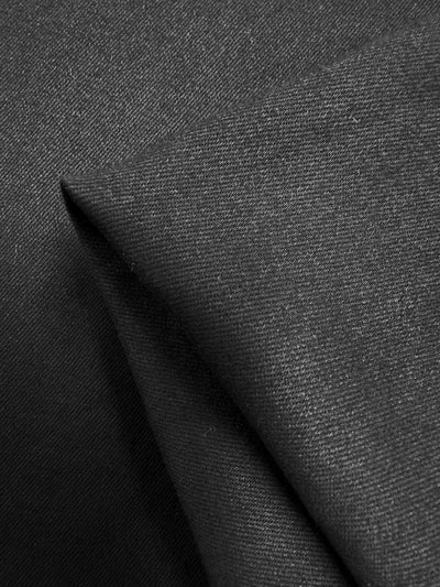 A close-up view of a neatly folded piece of Designer Stretch Denim - Black - 130cm from Super Cheap Fabrics. The texture is smooth with a fine weave that is visible. Subtle highlights and shadows give depth to the folds, emphasizing the fabric's substantial material and structure.