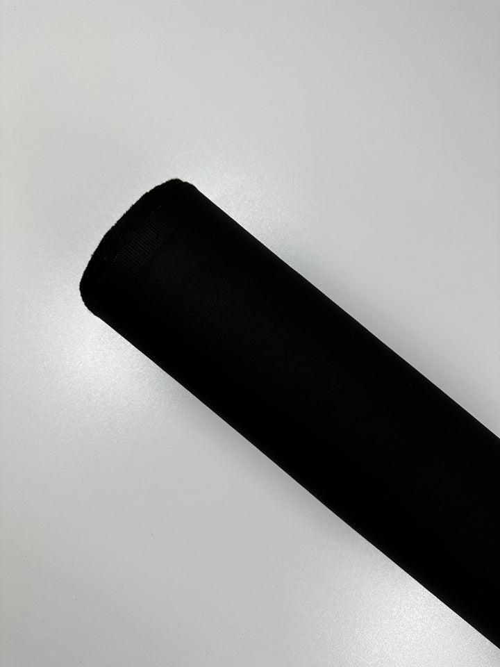 A close-up photo of a rolled-up piece of Designer Stretch Denim - Black - 130cm by Super Cheap Fabrics placed on a plain white background. The fabric is tightly rolled, with one end visible in the image, showing a smooth texture.