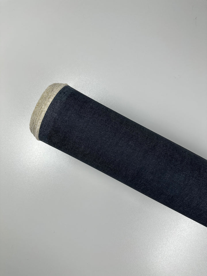 A rolled-up piece of Designer Denim - Classic - 170cm by Super Cheap Fabrics with a light beige edge is displayed on a plain white background. The heavy weight denim roll is partially unrolled, showcasing its texture and color.