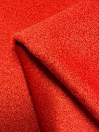 A close-up image of a folded red felt fabric. The heavy weight fabric has a smooth and soft texture, with a vibrant, spicy orange color. The fold in the fabric creates a slight shadow, adding depth to the image, making it perfect for outer coats. This is the Wool Cashmere - Spicy Orange - 150cm from Super Cheap Fabrics.