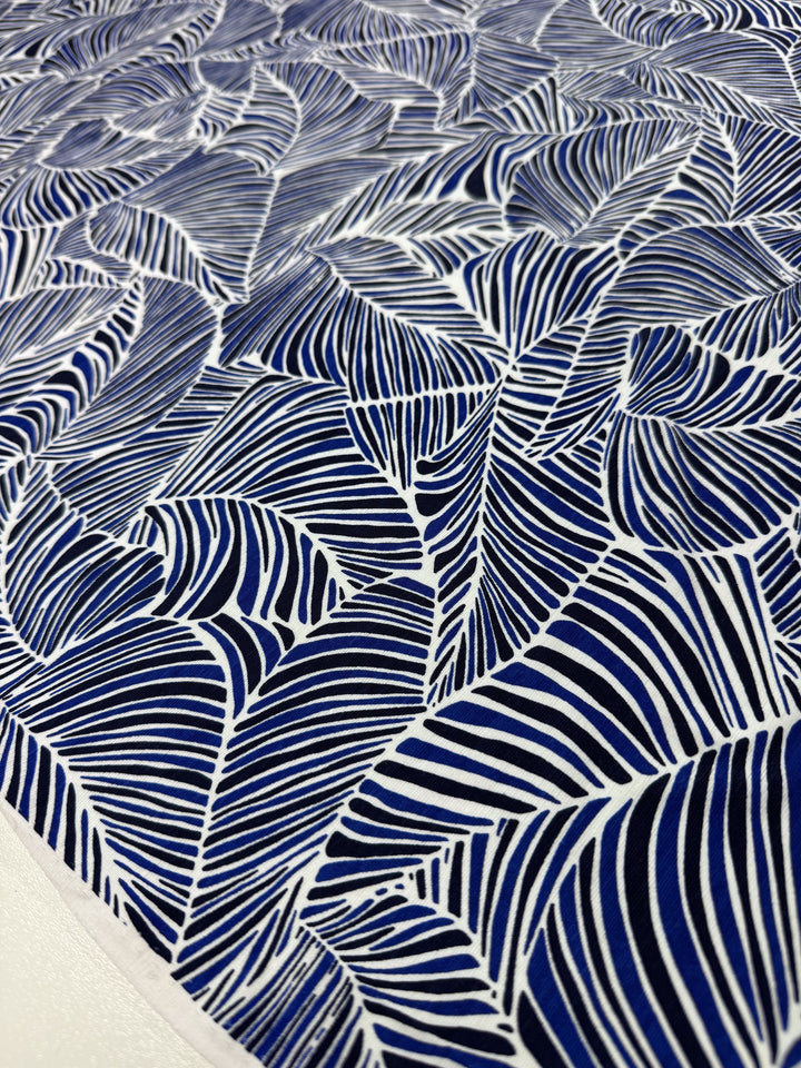 Close-up of Super Cheap Fabrics' Printed Lycra - Sapphire, 150cm wide, a blue and white medium-weight Polyester/Spandex blend featuring an abstract pattern with wavy lines resembling overlapping leaves or feathers, creating intricate organic shapes.