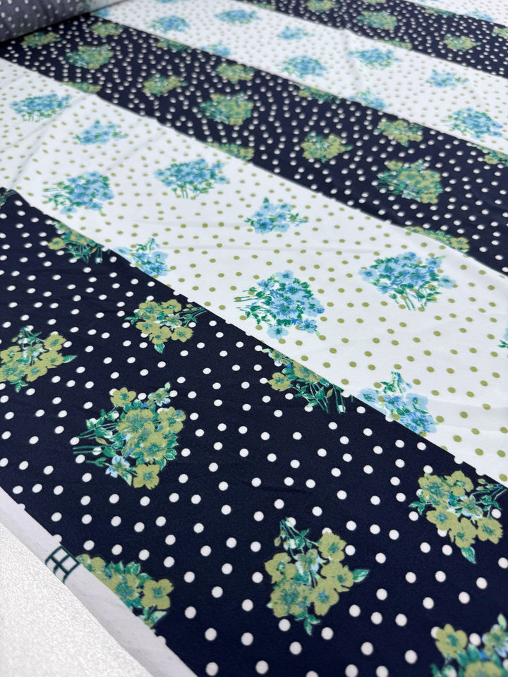 The Printed Lycra - Tea Party fabric by Super Cheap Fabrics, 150cm wide, features medium-weight stripes. Dark stripes boast green floral patterns with white polka dots, while light ones display green floral clusters and dots. This Polyester/Spandex blend is showcased flat for its vibrant design.