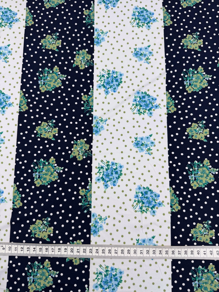 The Super Cheap Fabrics' Printed Lycra - Tea Party - 150cm features medium-weight Polyester/Spandex with alternating navy and white wide stripes. Navy stripes display white polka dots; white ones have blue and green floral patterns. A measuring tape at the bottom shows inches.