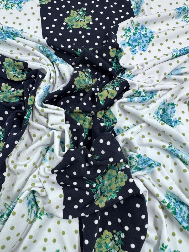 The "Printed Lycra - Tea Party - 150cm" by Super Cheap Fabrics is a medium-weight Polyester/Spandex blend with black and white polka dots, green floral designs, and small green spots on a white background, beautifully folded and draped for a layered texture.