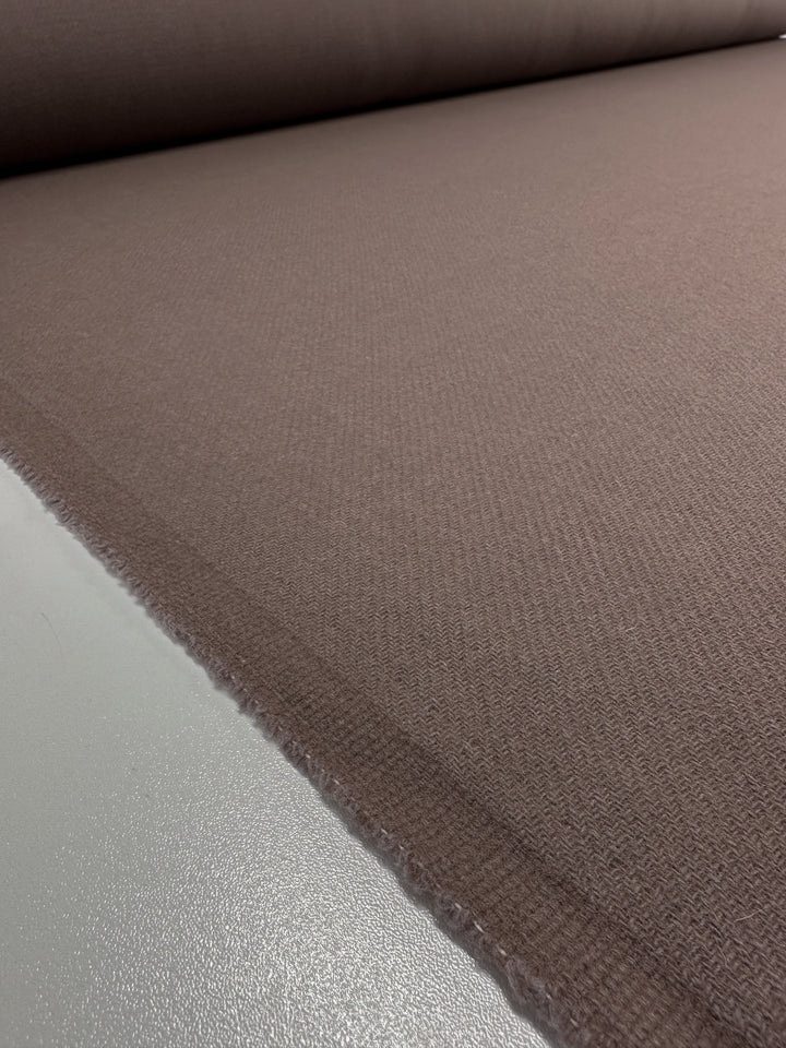 A roll of fabric laid out flat, displaying a smooth and even brown textile with a luxurious texture. The Super Cheap Fabrics Reversible Merino Wool - Antler - 150cm extends out horizontally, capturing the edge and a portion of the roll. The colors and texture are consistently uniform across the image.