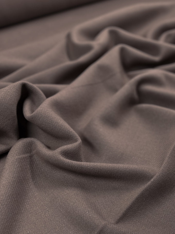 Close-up of a piece of crumpled brown fabric. The texture appears soft and smooth, with gentle folds and shadows creating a sense of depth and dimension. The lighting highlights the subtle details, enhancing the luxurious texture characteristic of Super Cheap Fabrics' Reversible Merino Wool - Antler - 150cm.