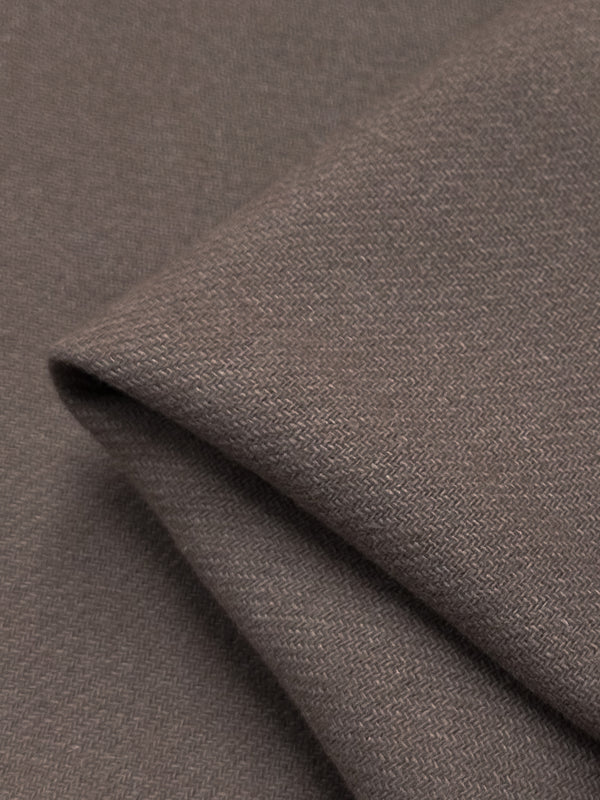 A close-up view of a piece of folded, textured brown fabric with a subtle herringbone pattern. The fabric's fine weave and gentle drape are visible, indicating the soft and smooth material typical of luxurious Reversible Merino Wool - Antler - 150cm by Super Cheap Fabrics.