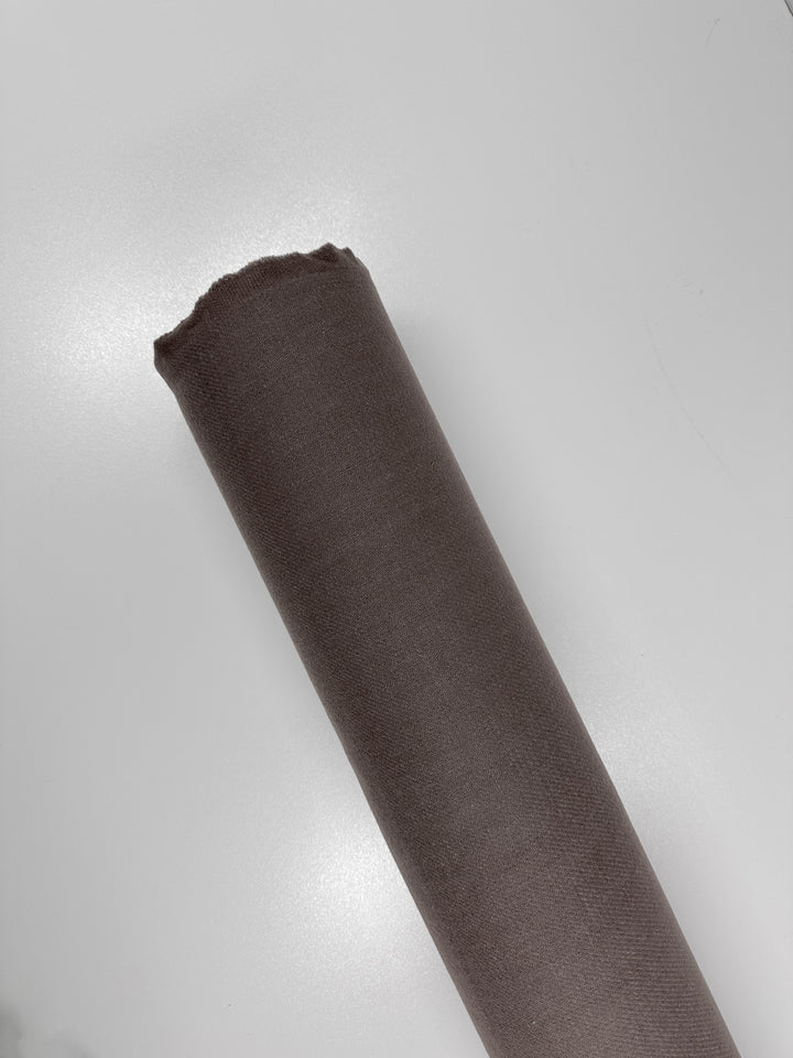 A rolled-up piece of brown fabric, made from Merino wool, is placed on a white surface. The luxurious texture and clean-cut end highlight its impeccable quality. This is the Reversible Merino Wool - Antler - 150cm by Super Cheap Fabrics.