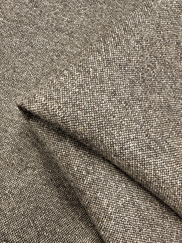 Close-up image of a folded piece of Super Cheap Fabrics' Wool Tweed - Speckled Brass - 147cm with a coarse, textured appearance. The fabric is woven in a tweed-like pattern, featuring a mix of neutral tones including gray and taupe. The intricate interweaving creates a speckled effect reminiscent of classic Italian textiles.
