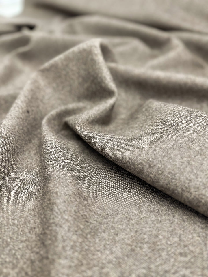 Close-up of a draped light brown Medium Weight Wool Tweed - Speckled Brass - 147cm by Super Cheap Fabrics with a soft texture and slight shimmer. The folds create a sense of depth and movement, highlighting its smooth and plush appearance.