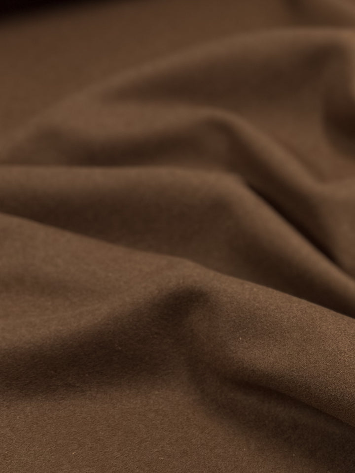 A close-up image of soft, brown Melton Wool - Caramel Cafe - 150cm by Super Cheap Fabrics with gentle folds and creases creating a wavy texture. The heavy weight wool fabric appears smooth and plush, highlighting the material's rich caramel cafe color and inviting texture.