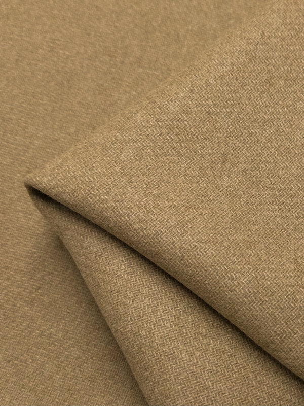 A close-up image of folded tan-colored fabric, made from Merino wool, with a subtle herringbone weave pattern. The texture appears soft and slightly textured, with gentle folds creating shadows and highlights on the surface, showcasing its natural breathability—*Reversible Merino Wool - Latte - 150cm* by *Super Cheap Fabrics*.