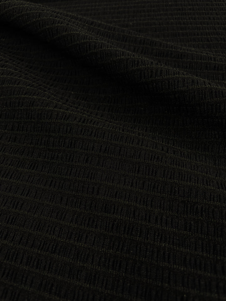 Close-up of the Designer Mesh - Black Rouge from Super Cheap Fabrics, featuring a dark green, lightweight grid-like pattern. The polyester spandex blend appears soft and slightly ridged, with light reflections highlighting its intricate texture. The image focuses on showcasing the detailed craftsmanship of this 130cm fabric.