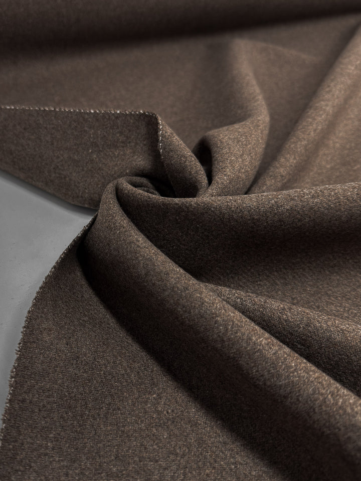 A close-up of Melton Wool - Shitake (150cm) by Super Cheap Fabrics shows its soft, textured brown surface, artfully draped to highlight flexibility and smoothness—ideal for creating luxurious outerwear.