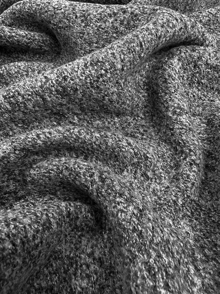 A close-up of a textured fabric, possibly heavy-weight Boiled Wool - Charcoal Marle - 140cm by Super Cheap Fabrics, in shades of gray. The fabric is arranged in soft, undulating folds that create a wavy and cozy appearance, perfect for autumn/winter clothing. The texture appears to be somewhat coarse with visible loops and fibers.