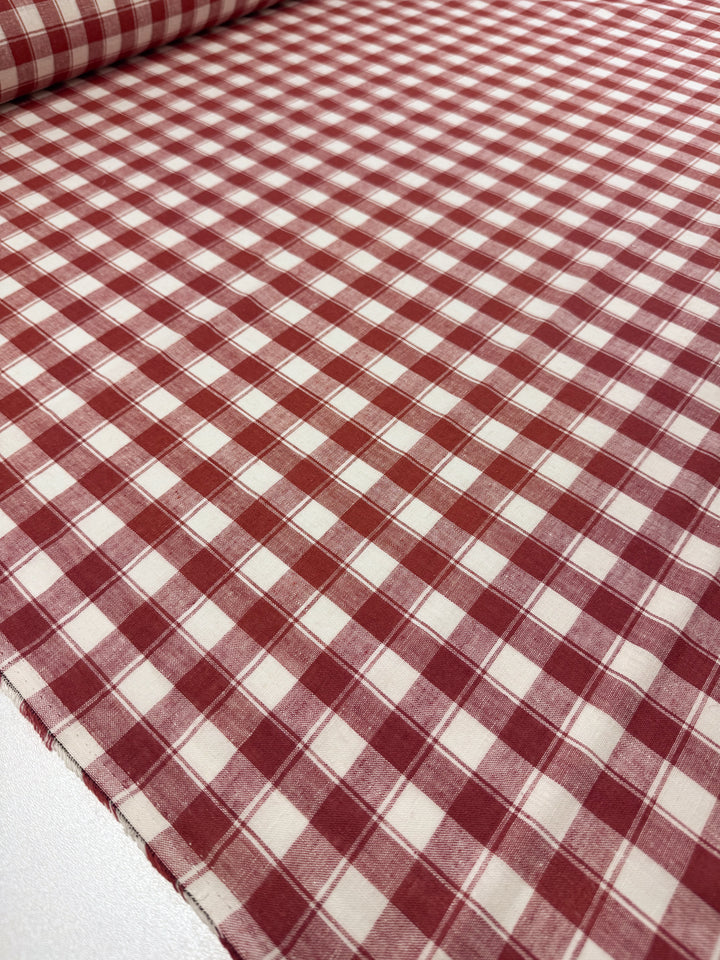 Super Cheap Fabrics' Linen Blend - Cranberry Check (145cm) is laid out flat, showing its lightweight material with evenly spaced red and white squares. The fabric roll appears at the top edge of the image.