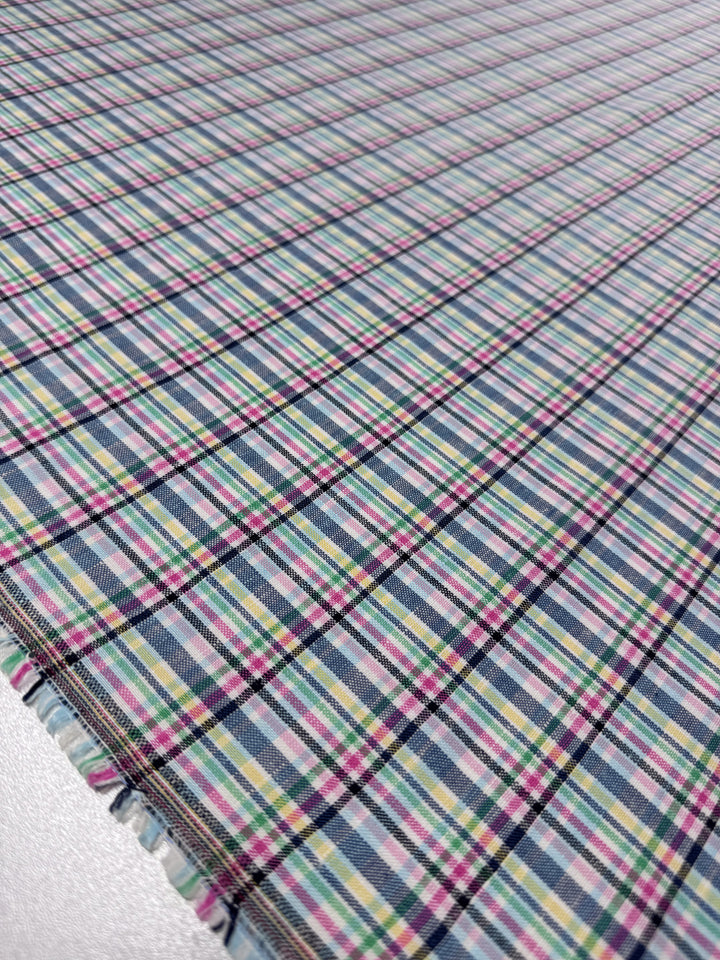 A close-up of Super Cheap Fabrics' Linen Blend - Tartan Prism (140cm) shows its lightweight linen cotton blend in a vibrant blue, pink, yellow, green, and black tartan plaid pattern, displayed flat with the fabric edge visible.