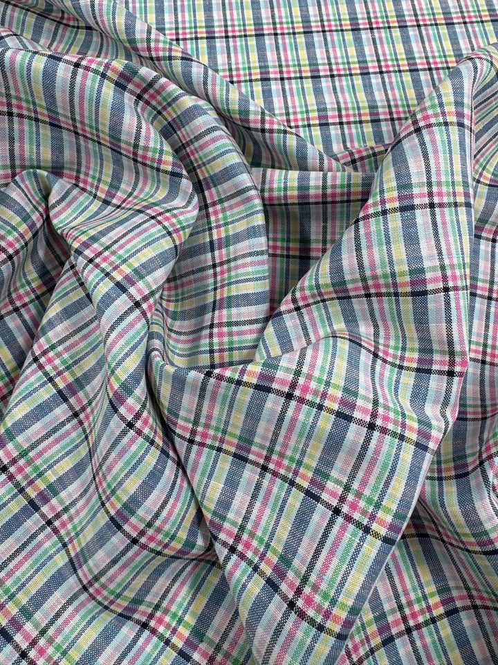 A close-up of Super Cheap Fabrics' Linen Blend - Tartan Prism (140cm) shows a lightweight, softly gathered linen with a vibrant checkered plaid of blue, pink, green, yellow, and black intersecting lines.