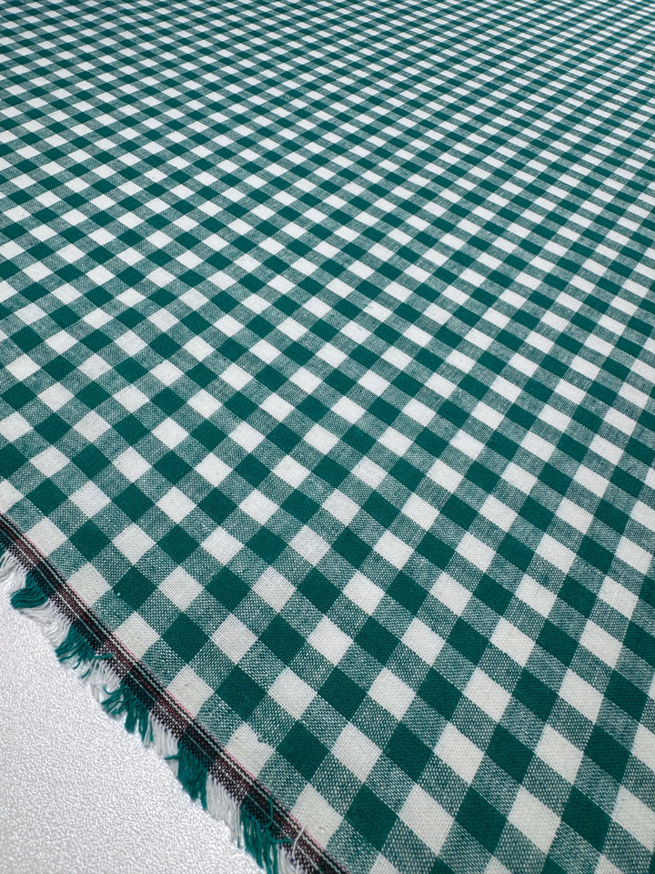 A close-up of Super Cheap Fabrics’ Linen Blend - Verdant Gingham (145cm) shows its green and white checkered lightweight texture with frayed edges, displayed flat on a light surface.