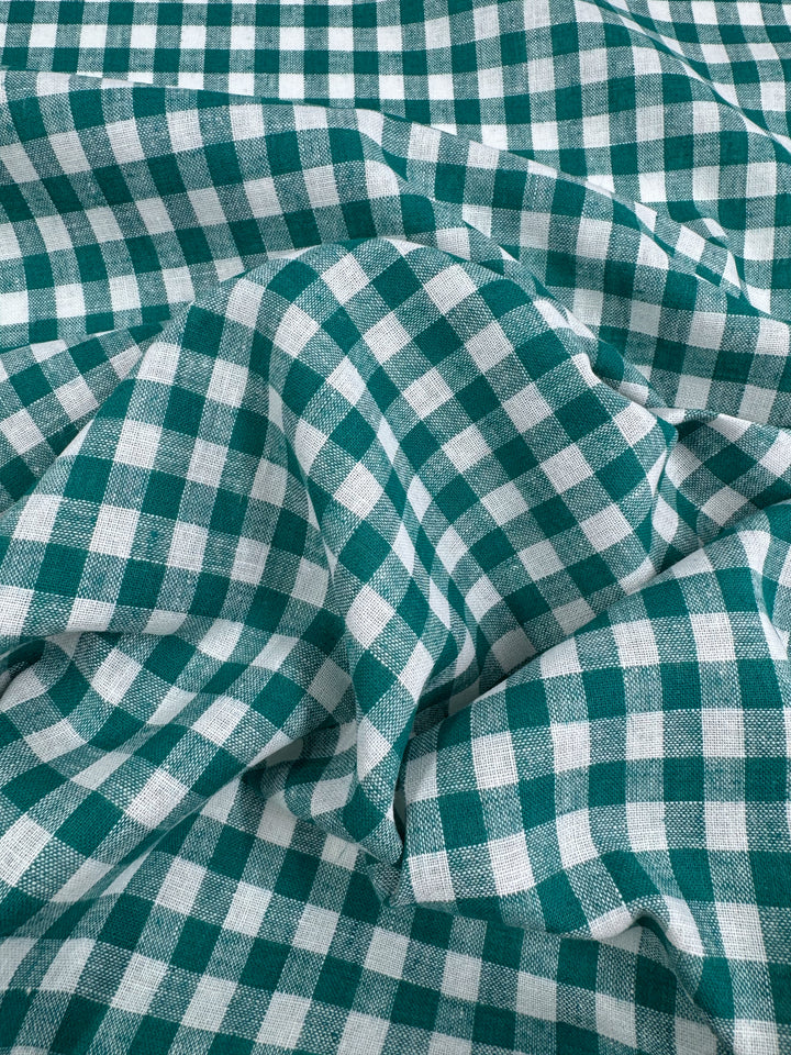 Lightweight and verdant green, Super Cheap Fabrics' Linen Blend - Verdant Gingham - 145cm features a green and white checkered gingham pattern, shown with soft folds and creases.
