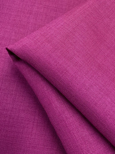 A close-up of Twill Suiting - Fuchsia Rose by Super Cheap Fabrics shows its folded, textured surface with visible diagonal lines and a smooth, slightly shiny finish; fabric width is 150cm.