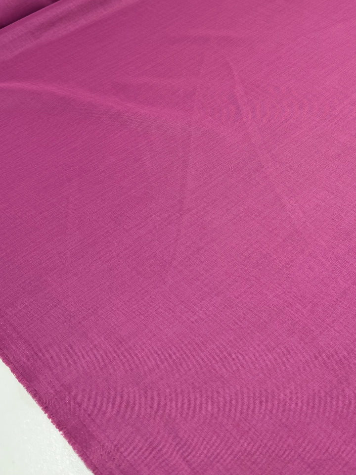 A close-up of Super Cheap Fabrics’ Twill Suiting in Fuchsia Rose (150cm) shows the smooth polyester surface, fine texture, subtle creases, and distinct diagonal weave.