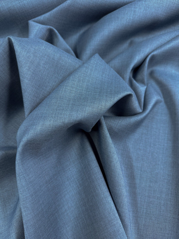 A close-up of Super Cheap Fabrics' Twill Suiting - Bluesteel (150cm), featuring light blue fabric with a smooth texture and diagonal weave, shown in soft folds and gentle creases.